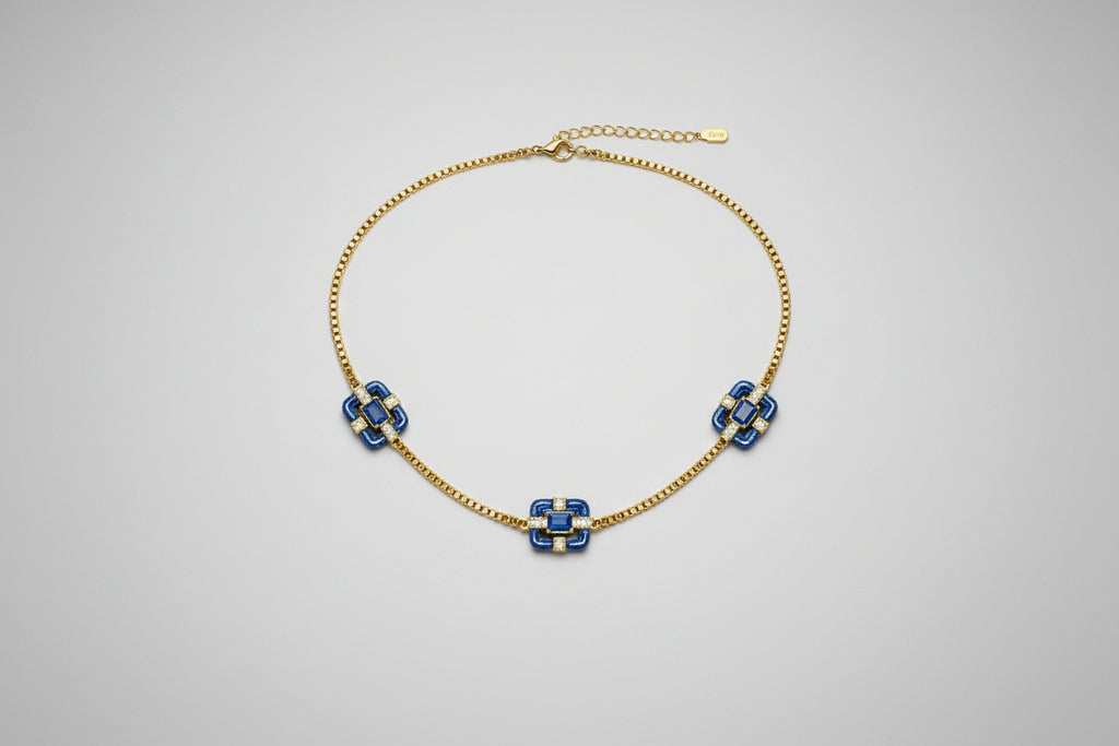 A delicate gold chain necklace featuring three small floral motifs, each accented with blue stones.