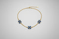 A delicate gold chain necklace featuring three small floral motifs, each accented with blue stones.