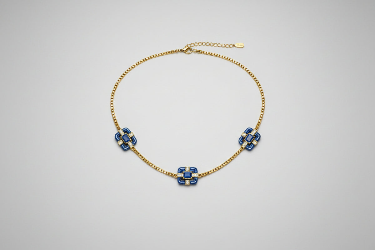 A delicate gold chain necklace featuring three small floral motifs, each accented with blue stones.