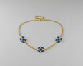 A delicate gold chain necklace featuring three small floral motifs, each accented with blue stones.
