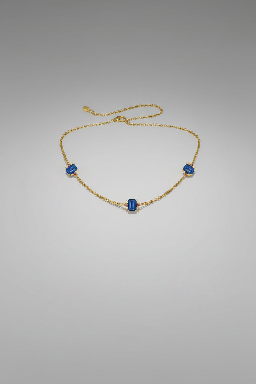 A delicate gold chain necklace featuring three small square-cut blue gemstones.
