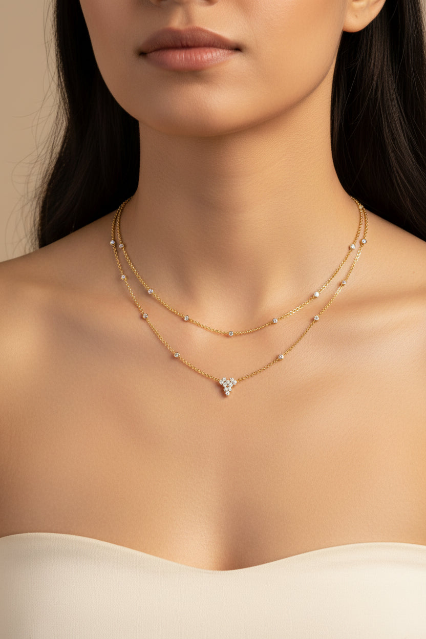 A delicate two-layer gold necklace with small white gemstone accents and a central floral cluster pendant.