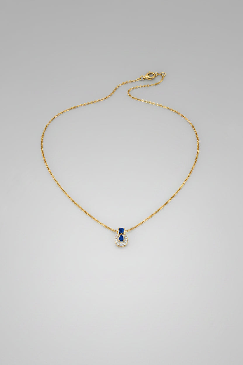A delicate gold chain necklace with a small teardrop-shaped pendant featuring a white inlay and a tiny blue accent.