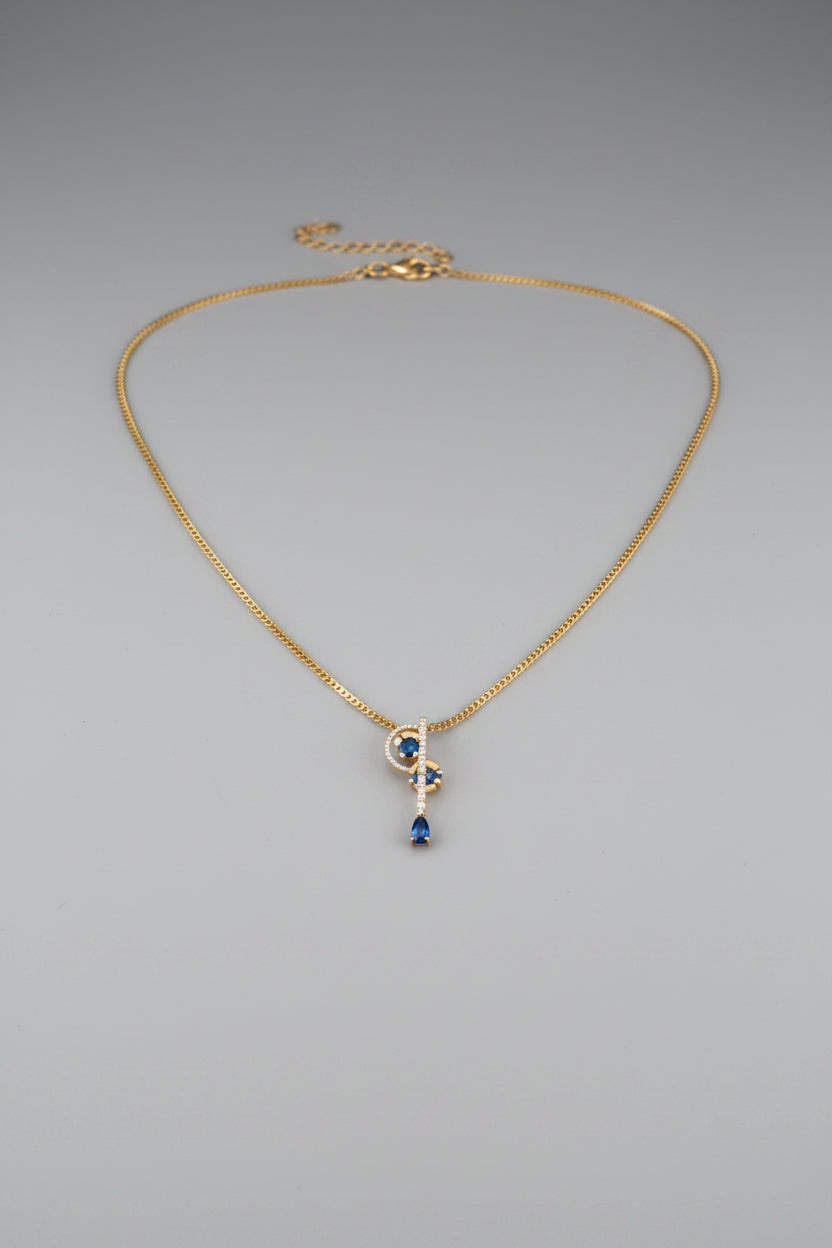 A delicate gold chain necklace with a small circular pendant featuring a vertical blue drop.