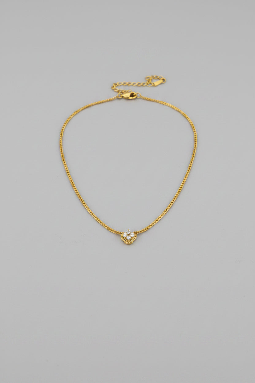 A delicate gold chain necklace with a small, clear, diamond-like heart-shaped pendant.