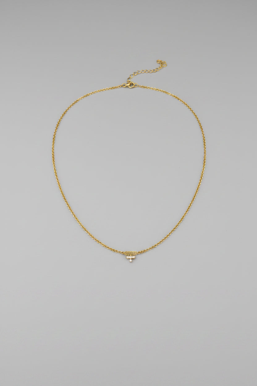 A delicate gold chain necklace with a small geometric pendant, displayed against a solid black background.