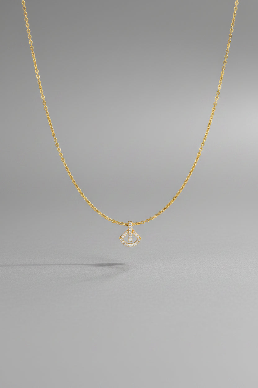 A delicate gold chain necklace with a small pendant featuring a white central bar and a gold crescent moon shape.
