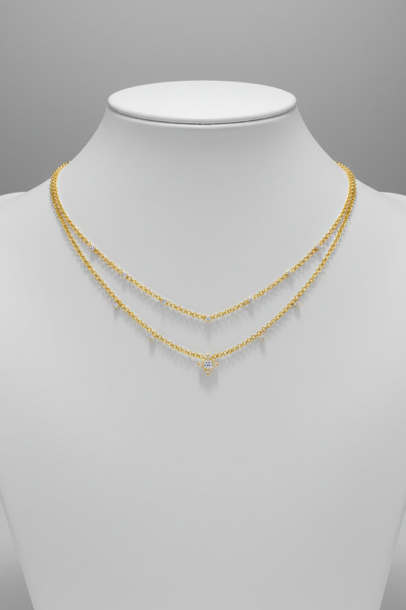 A delicate double-layered gold necklace with small sparkling stones and a central diamond-shaped pendant.