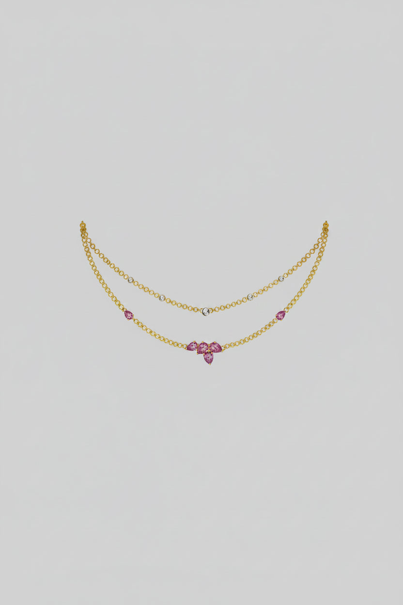 A delicate double-strand gold necklace with small white gemstone accents and a central pink gemstone bow-shaped pendant.