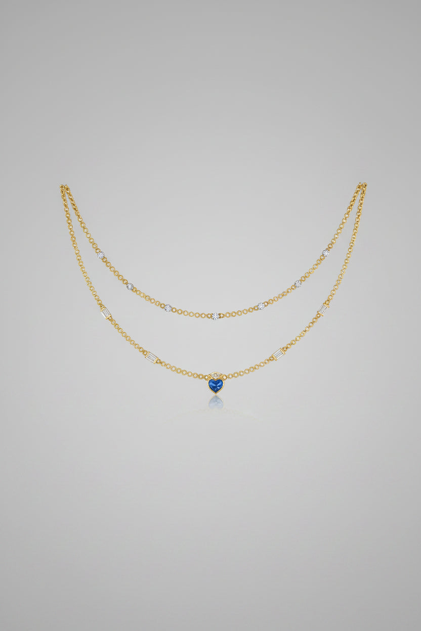 A delicate double-layered gold necklace with small clear stones and a central round blue gemstone.