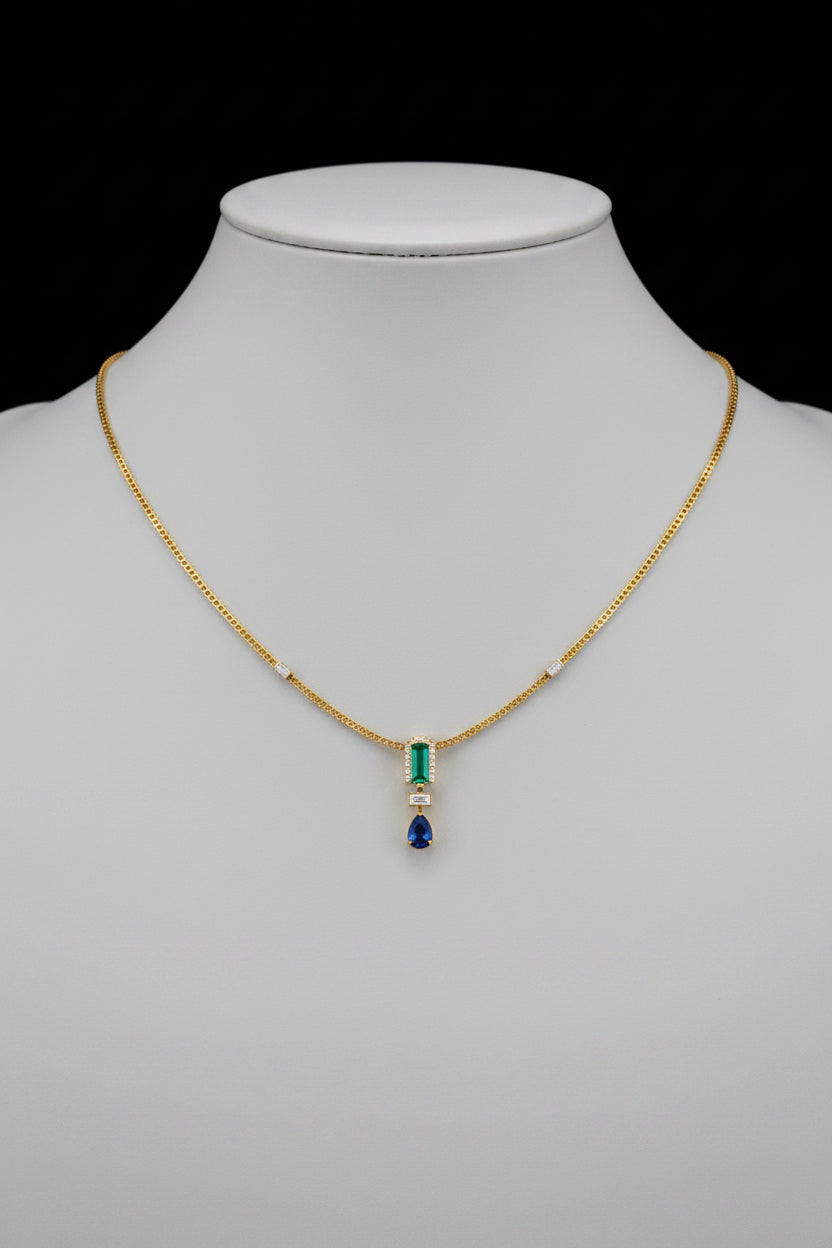 A delicate gold necklace with a central pendant featuring a light blue rectangular stone, a small gold accent, and a dangling blue teardrop gemstone.