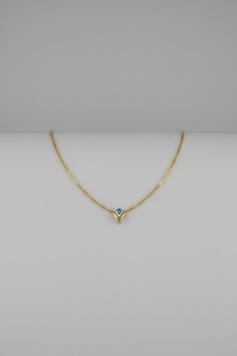 A delicate gold necklace with a small blue gemstone pendant, centered on a solid black background.